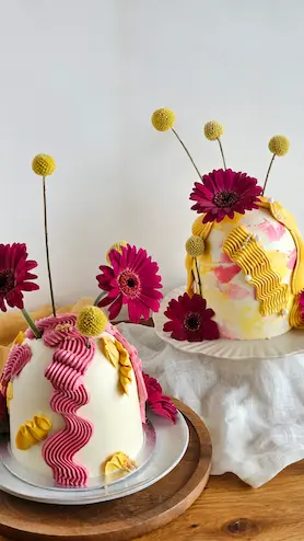 Two dome cakes decorated with pink and yellow buttercream and fresh flowers